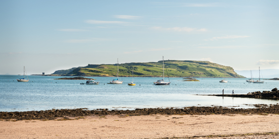 People on the beach in Millport with boats moored in Millport bay, Cumbrae, Scotland